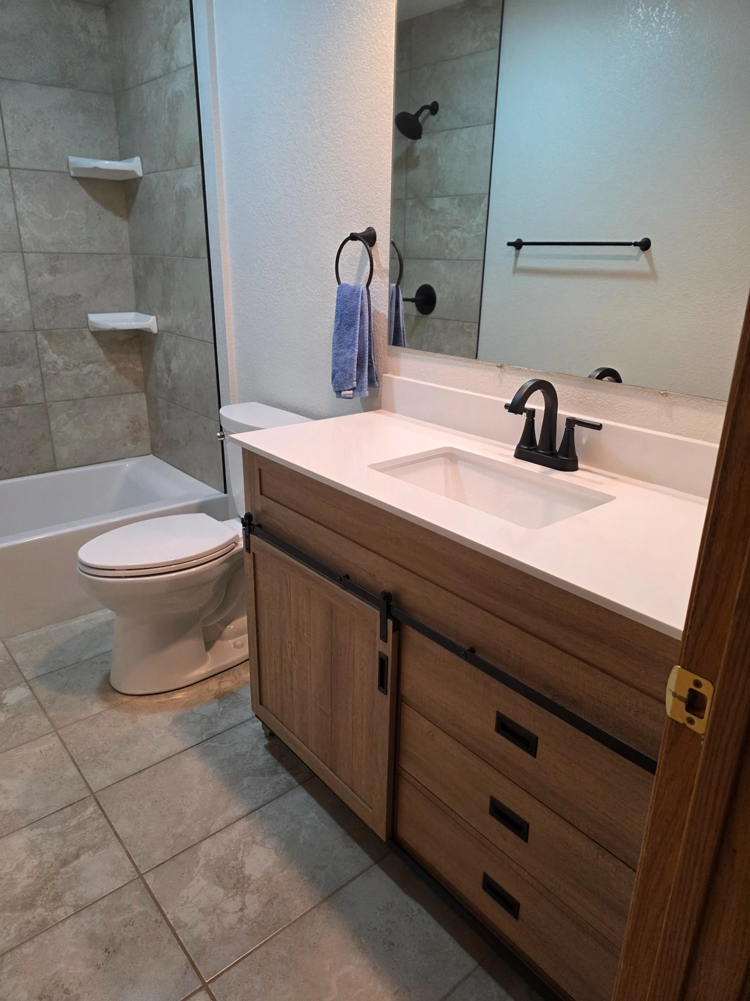 Finished bathroom remodel with wood vanity, quartz top and tiled tub surround